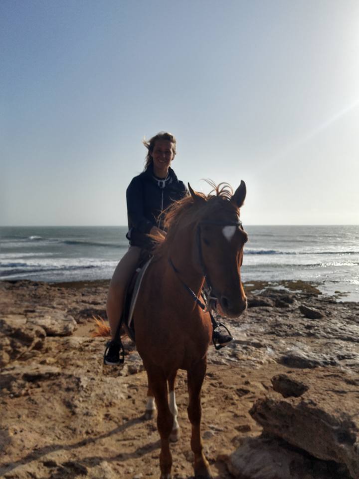 girl sitting on the back of horse at the beach
